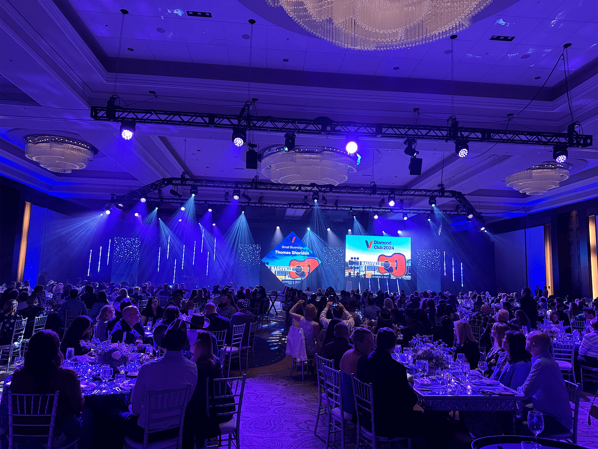 A brightly lit gala event featuring elegantly dressed attendees seated at tables, with a stage displaying "Diamond Club 2024" in Nashville.